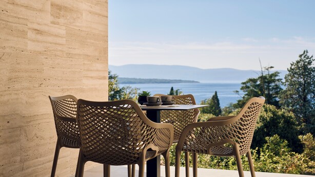 A table with four chairs and a small plant, set against a backdrop of a clear sky and distant mountains. - Malinska Green Apartments (Malinska-Dubasnica)