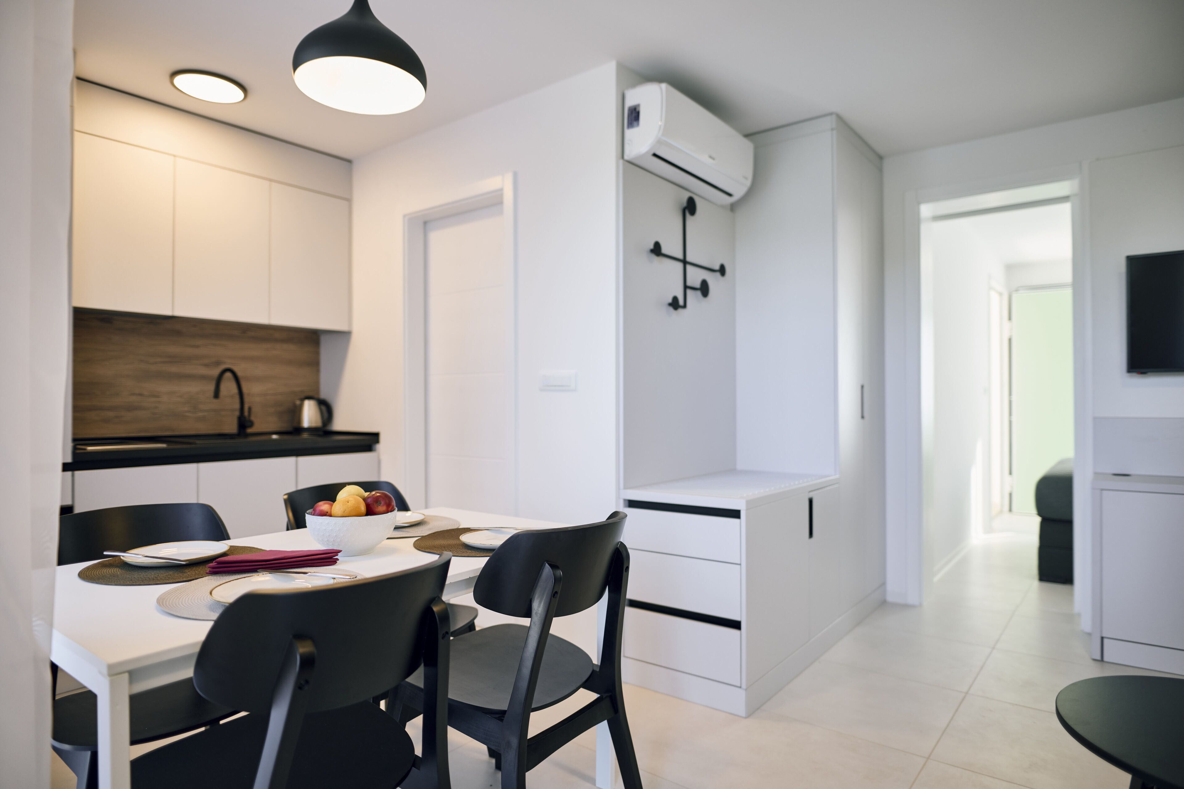 Et moderne køkken med hvide skabe, en sort bordplade og en indbygget aircondition.