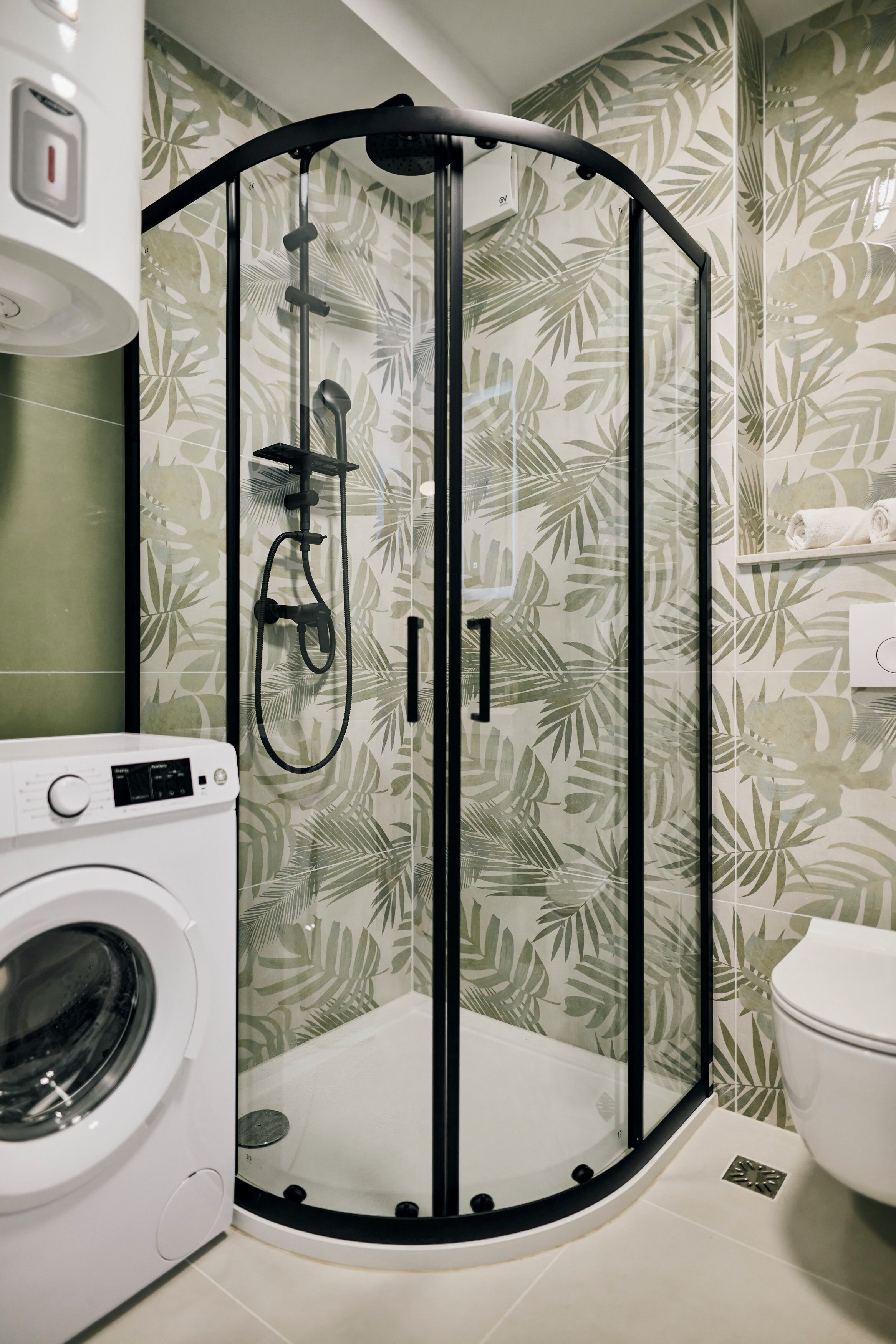 A compact bathroom with a glass-enclosed shower, a washing machine, and a toilet.