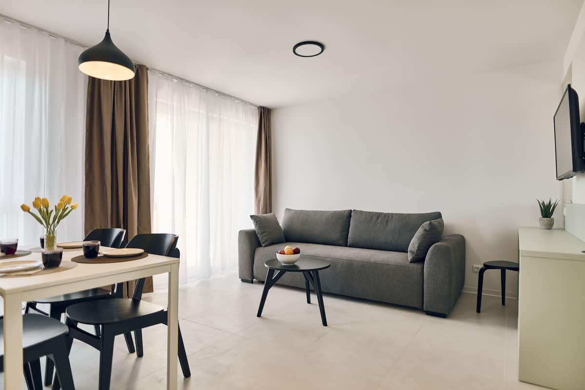 Ein modernes Wohnzimmer mit grauem Sofa, einem Esstisch mit Stühlen, einem kleinen Beistelltisch und einer Pendelleuchte.