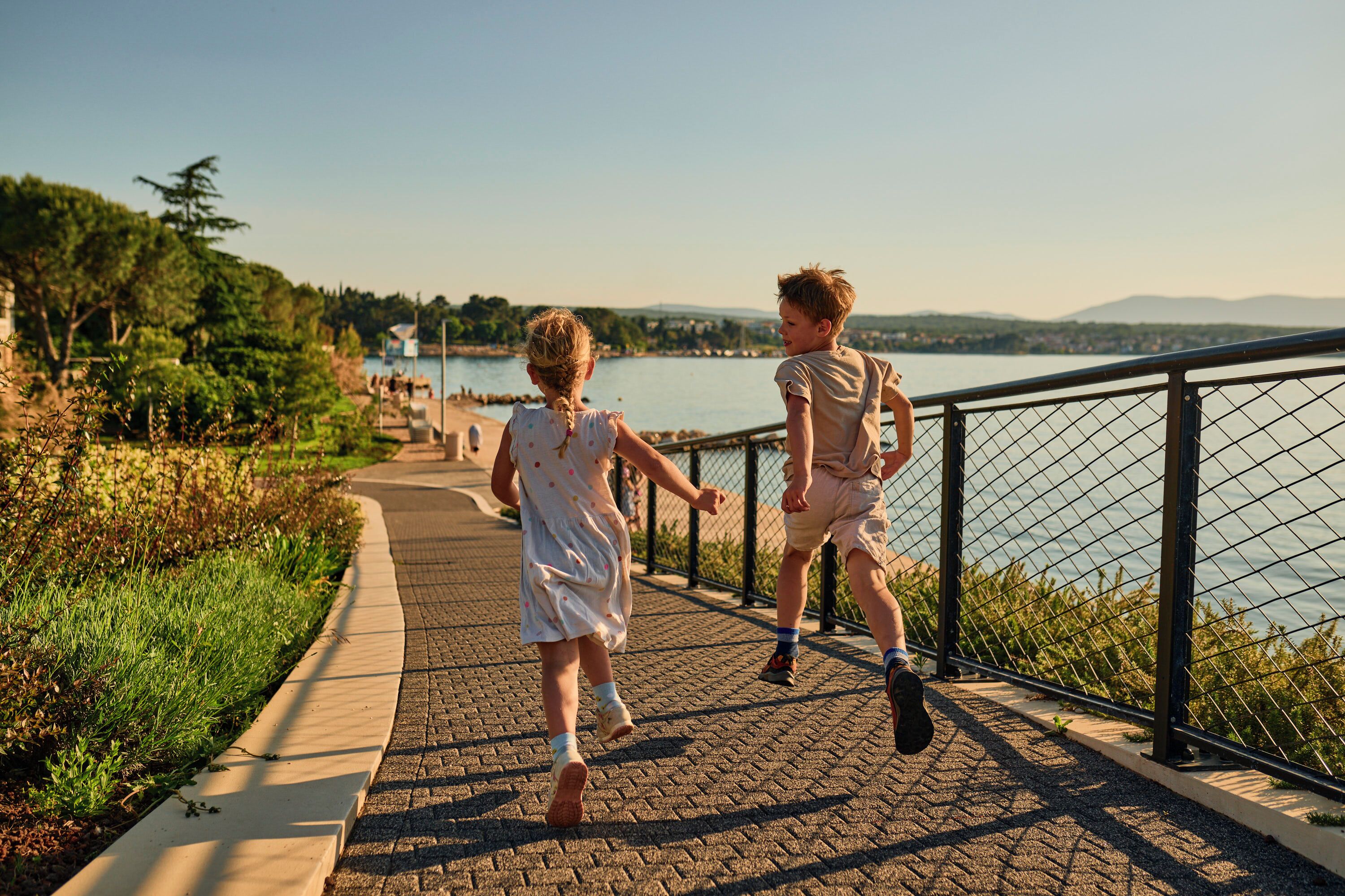 A paved walkway beside a body of water, with a metal railing on one side.