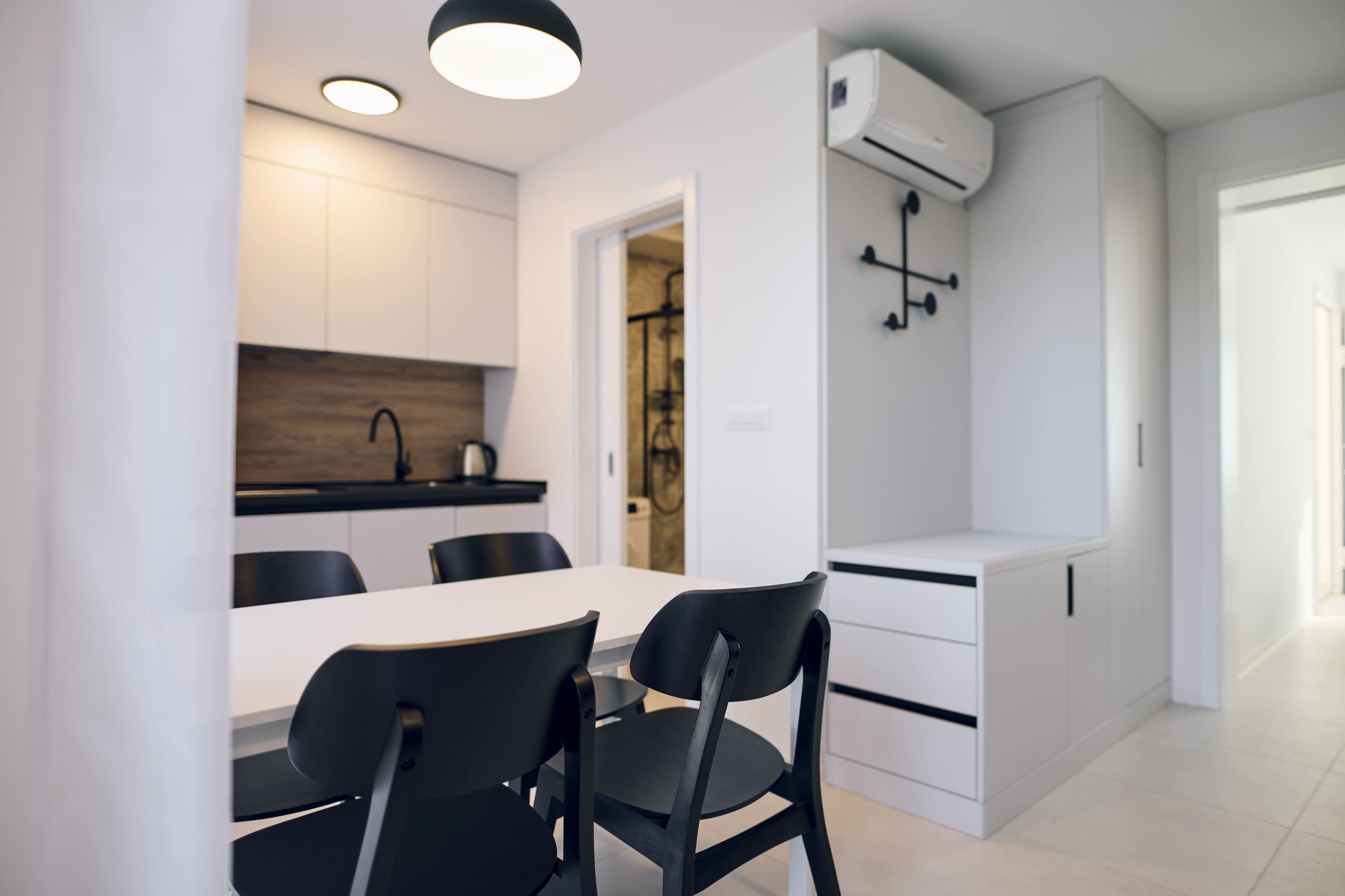 Une cuisine moderne avec des meubles blancs, des chaises noires et un plan de travail blanc.
