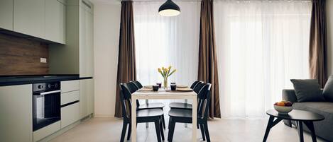 A modern kitchen with a dining area, a sofa, and a small table with fruit.