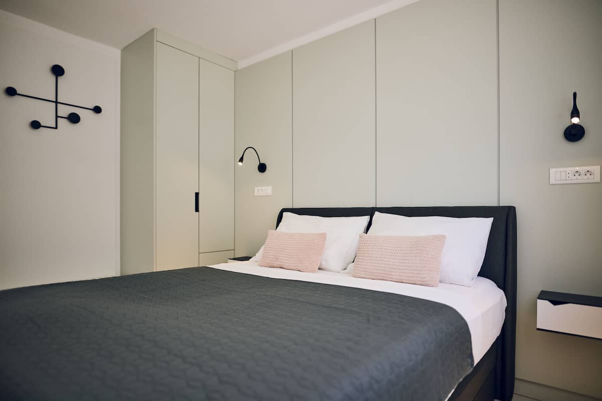 Ein modernes Schlafzimmer mit einem großen Bett, einem Kleiderschrank, einem Nachttisch und einer Wandleuchte.