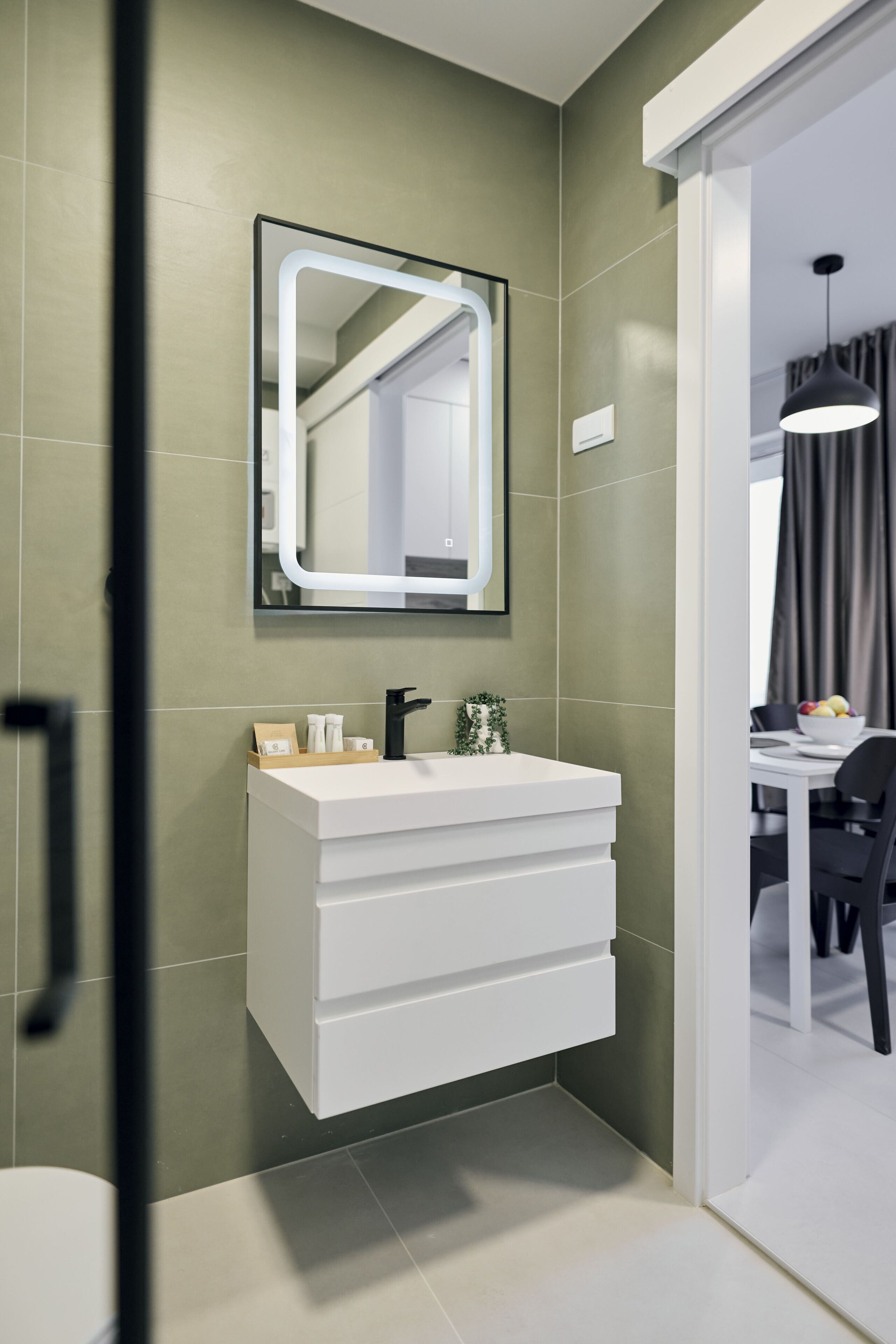 Une salle de bain moderne avec un meuble-lavabo blanc, un grand miroir et un mur vert.