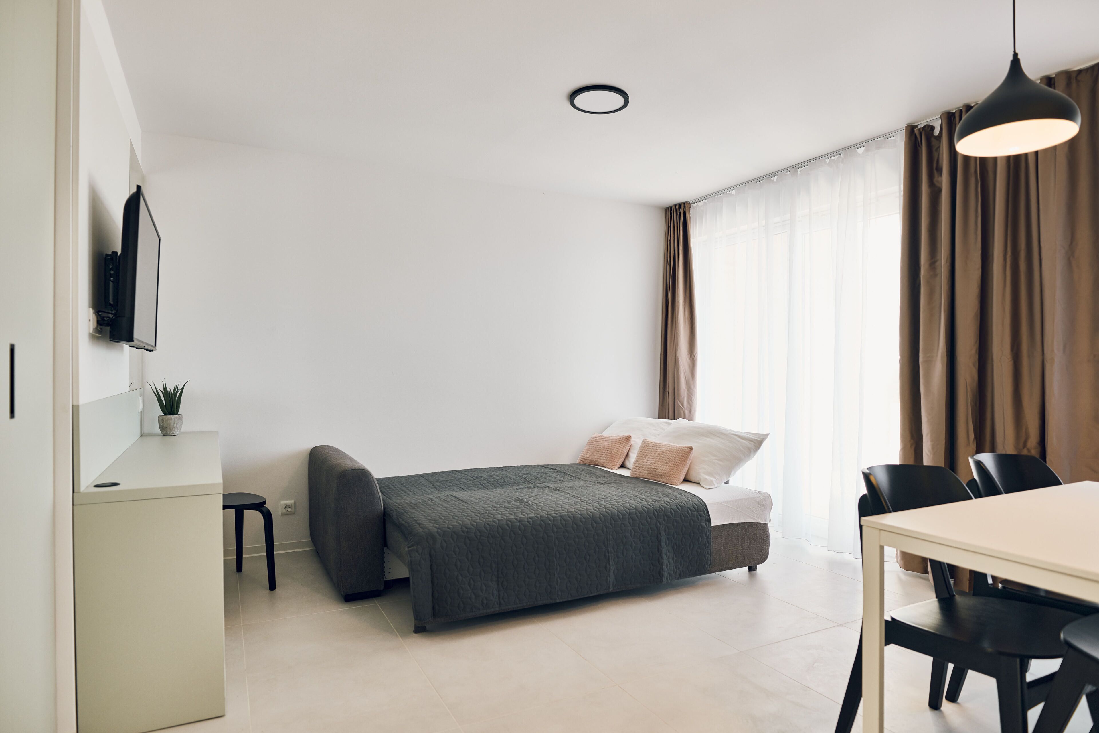 Une chambre à coucher moderne et minimaliste, comprenant un lit, une table de chevet et un espace bureau.