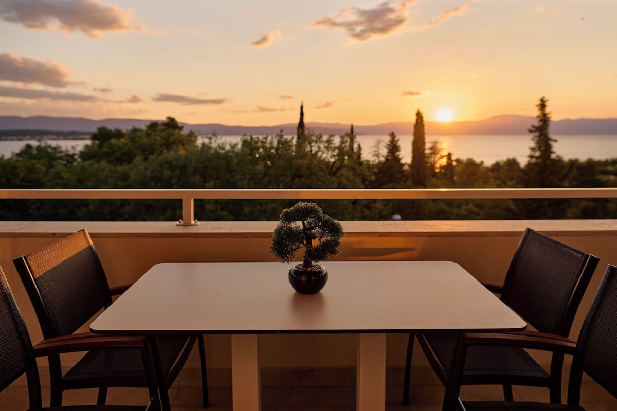 Ein Balkon mit Tisch und Stühlen, der einen schönen Blick auf Bäume und Berge bei Sonnenuntergang bietet.