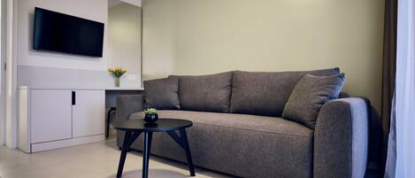 A modern living room with a grey sofa, a small black table, and a flat-screen TV mounted on the wall.