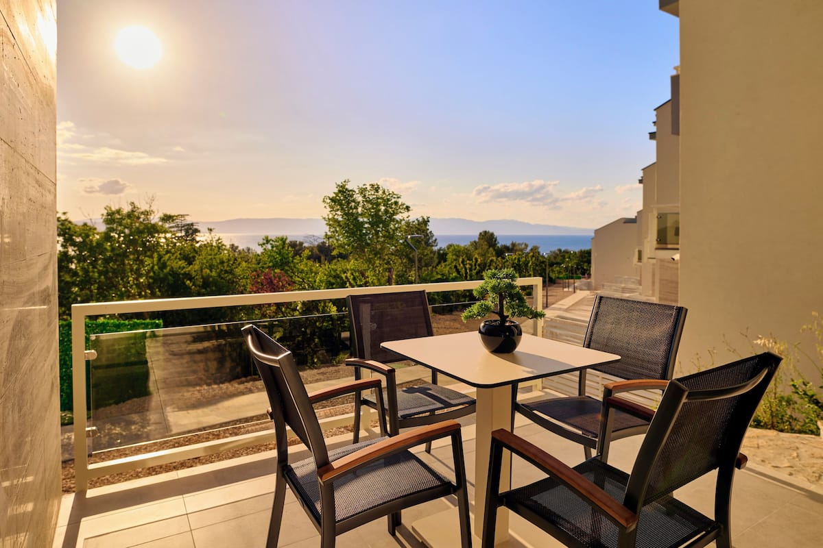 Ein Balkon mit Tisch und Stühlen, der auf eine reizvolle Landschaft mit Bäumen und Bergen blickt.