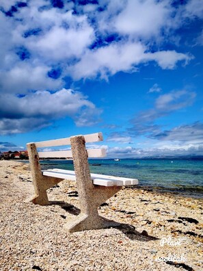 Eine Betonbank an einem Kiesstrand mit freiem Blick auf Meer und Himmel.