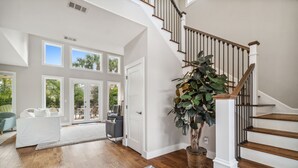 Un vaste salon doté de parquet, d’un escalier et de grandes fenêtres donnant sur un jardin.