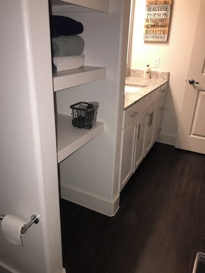 Un baño con un dispensador de papel higiénico, un perchero con toallas dobladas, una cesta y una encimera con dispensador de jabón.