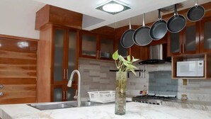 A kitchen with wooden cabinets, a marble countertop, a sink, a stove, and hanging pots. - Casa Real con tobogán de agua privada (San Miguel de Cozumel)