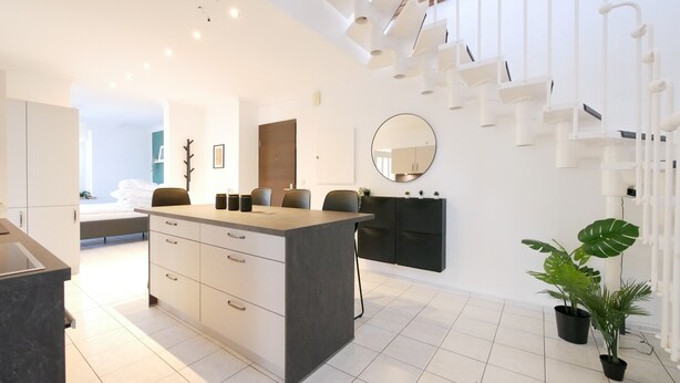 Una cocina moderna con una isla central, muebles blancos y una escalera que lleva a un nivel superior.