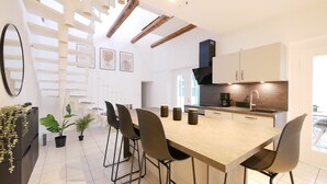 Una cocina moderna con una isla central, taburetes de bar y una escalera que lleva a un nivel superior.