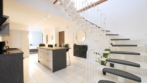 Una cocina moderna con una isla central, una escalera con barandillas blancas y un comedor con sillas y una mesa.