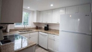 Una cocina moderna con armarios blancos, un lavamanos de acero inoxidable, lavavajillas y refrigerador.