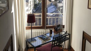 A room with a large window, a table with a chair, a red lamp, and a radiator.