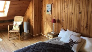 A cozy room with wooden walls, a bed with a deer pillow, a chair with a floral cushion, and a poster on the wall.