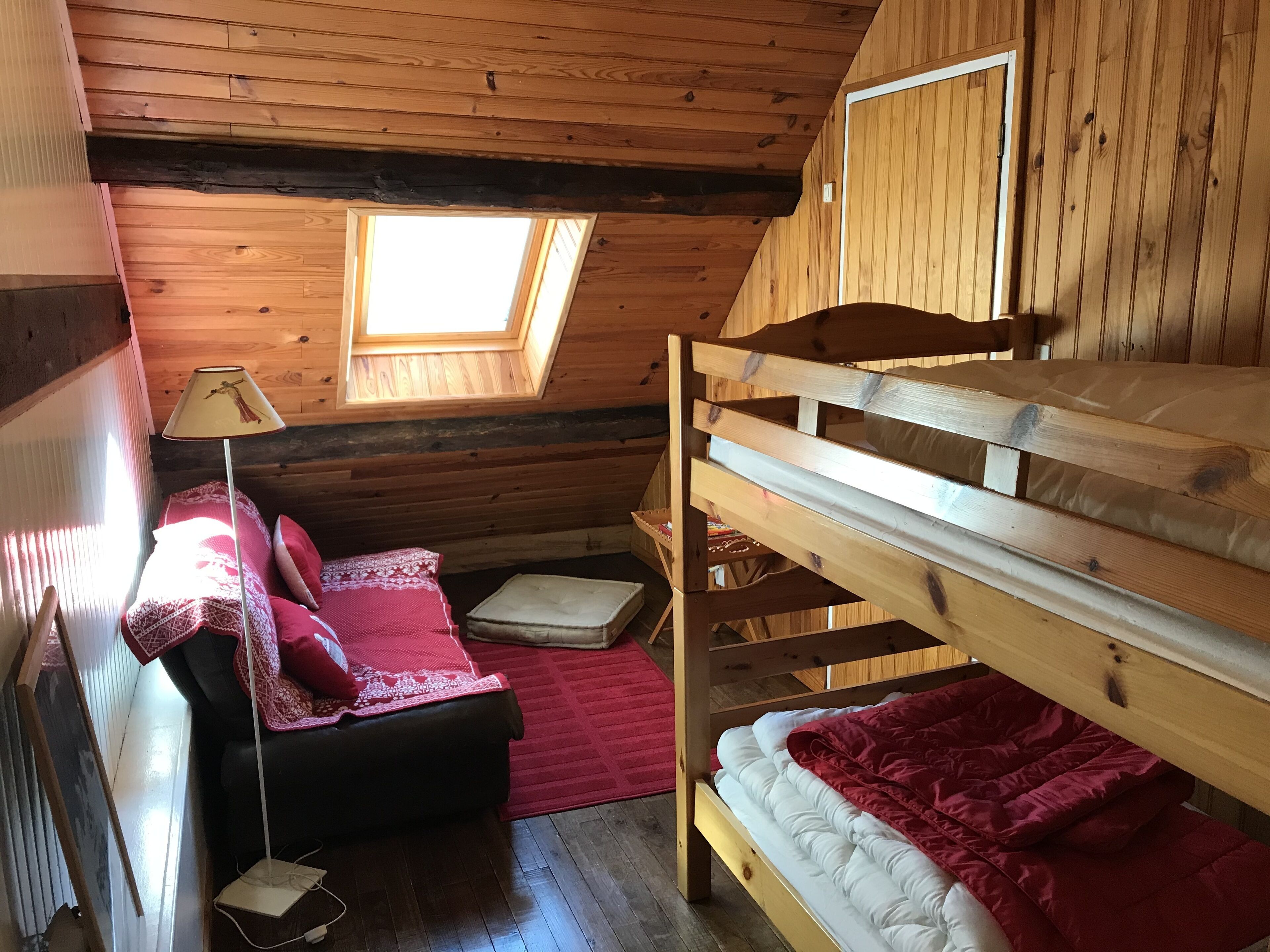 Een knus kamer in een chalet met een stapelbed, een bureau met lamp en een dakraam.