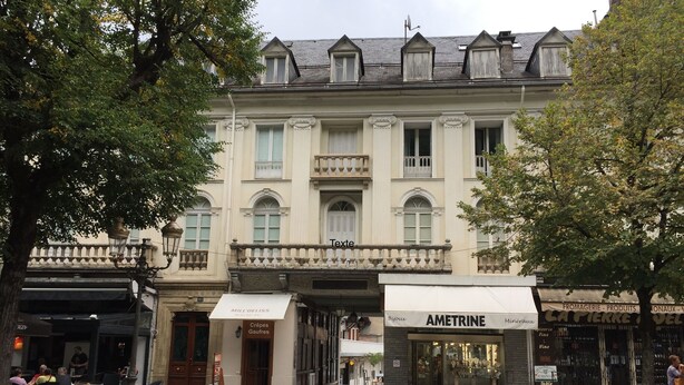 A building with a classic European architectural style, featuring a balcony with ornate railings and multiple windows with shutters.