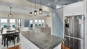 A spacious kitchen with a large island, stainless steel refrigerator, and pendant lighting.