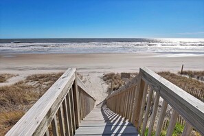 A wooden boardwalk leading to a beach with a clear view of the ocean.