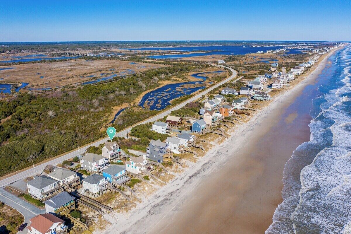 A coastal residential area with houses along the beach, a road, and a bridge in the background.