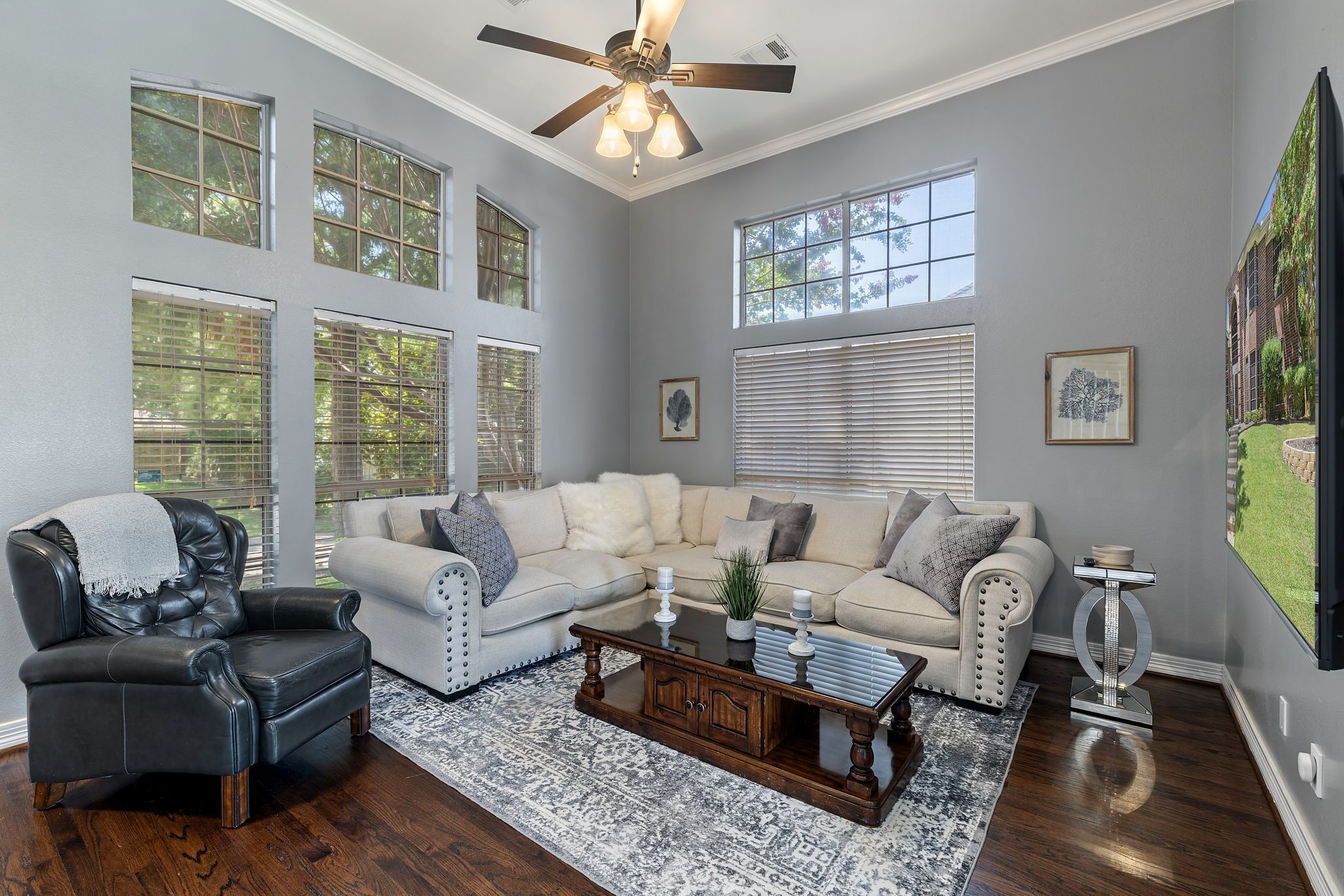 A living room with a leather armchair, a beige sectional sofa, a wooden coffee table, and a ceiling fan.