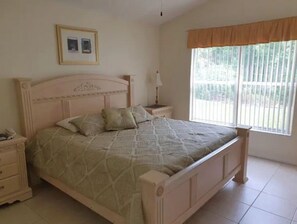 A bedroom with a bed, nightstands, a lamp, a window with blinds, and a framed picture on the wall. - Poolside Sunny Retreat (Kissimmee)
