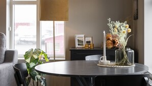A dining area with a round table, black chairs, a potted plant, a tall floor lamp, and a vase with dried flowers. - Keflavik's Ray of sunshine Hafnargata (Reykjanesbær)
