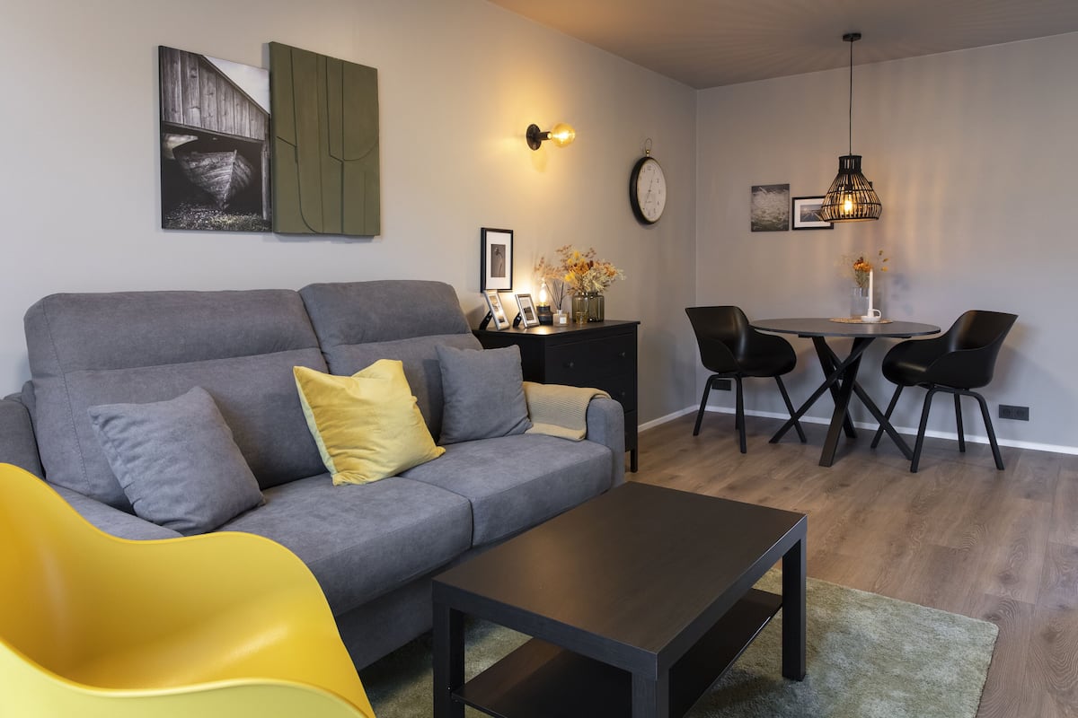 A modern living room with a grey sofa, yellow chair, and a dining area with a round table and chairs.