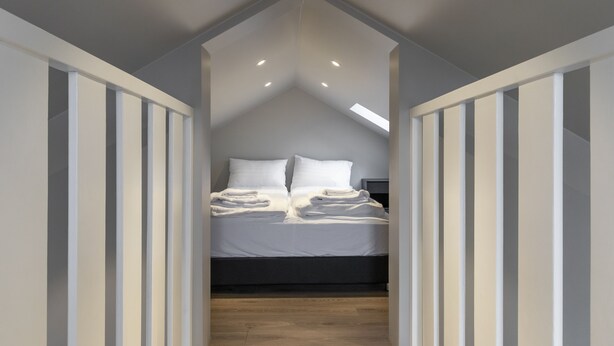 A bedroom with a sloped ceiling, a bed with white linens, and a wooden floor. - Keflavik's Ray of sunshine Hafnargata (Reykjanesbær)