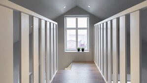 A narrow hallway with a sloped ceiling and a large window at the end. - Keflavik's Ray of sunshine Hafnargata (Reykjanesbær)