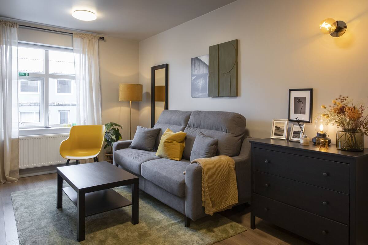 A modern living room with a grey sofa, a yellow chair, a dark wooden coffee table, and a black dresser.