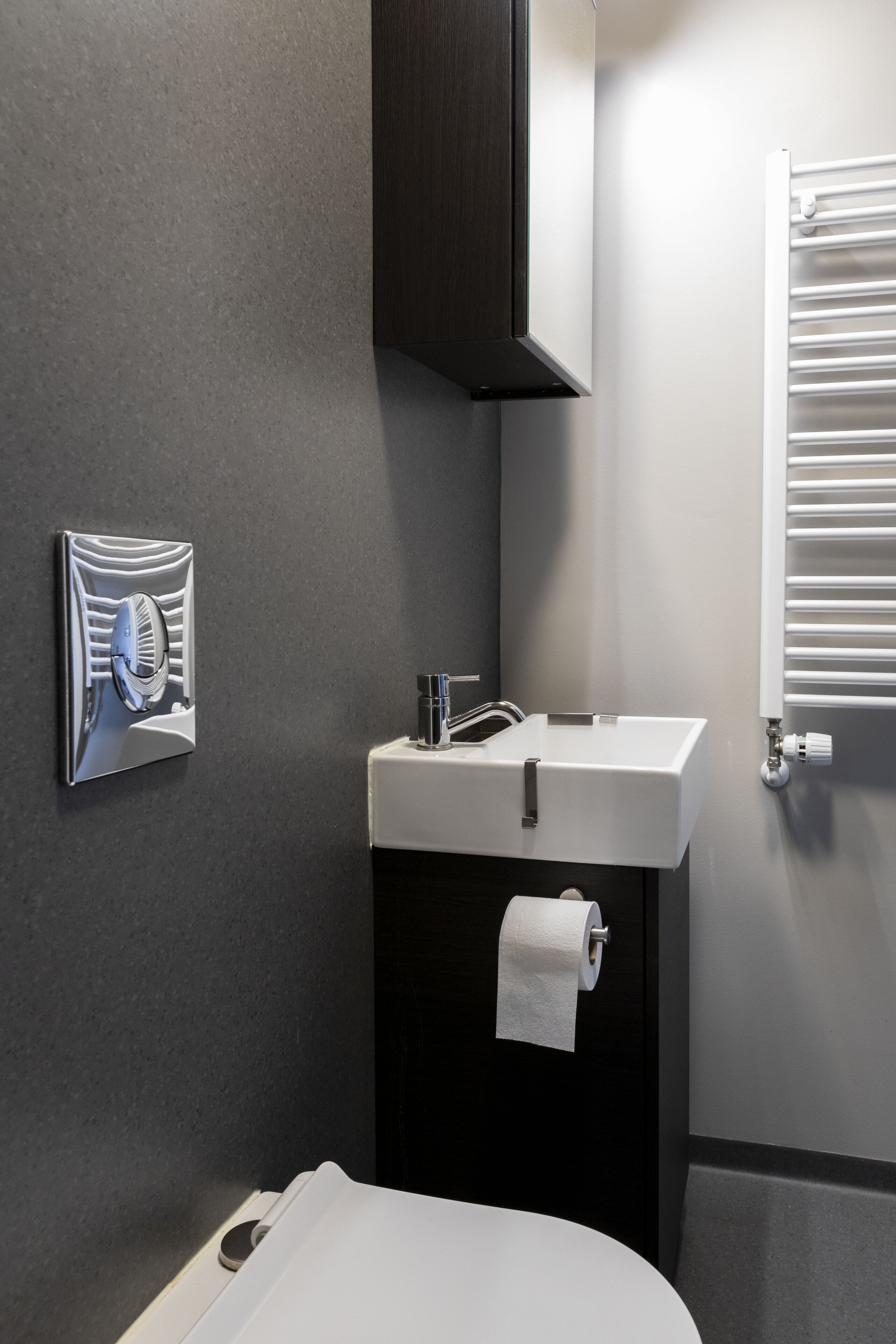 A modern bathroom with a white sink, dark cabinet, and a towel hanging on the wall.