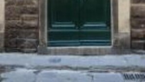 Eine grüne Doppeltür mit einem halbkreisförmigen Fenster darüber, in eine Fassade aus Stein gebaut.