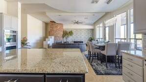 A modern kitchen with granite countertops, a built-in oven, and a dining area with a gray sofa and dining table. - Pristine Luxury Estate, Views, Sleeps 26, Heated Pool & Spa (Fountain Hills)