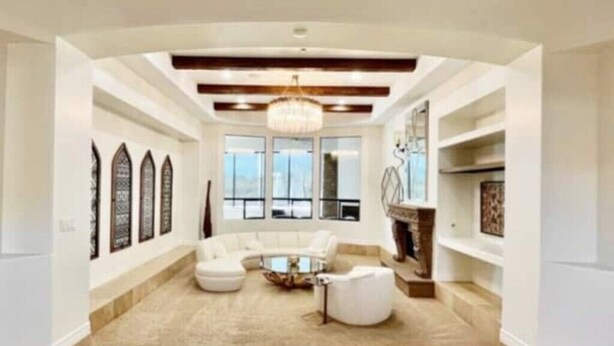 A spacious living room with a large L-shaped sectional sofa, a coffee table, and a fireplace. There are large windows providing natural light and a view of the outdoors. - Pristine Luxury Estate, Views, Sleeps 26, Heated Pool & Spa (Fountain Hills)