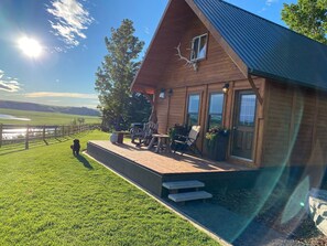 A wooden cabin with a porch, outdoor seating, and a view of a lake.