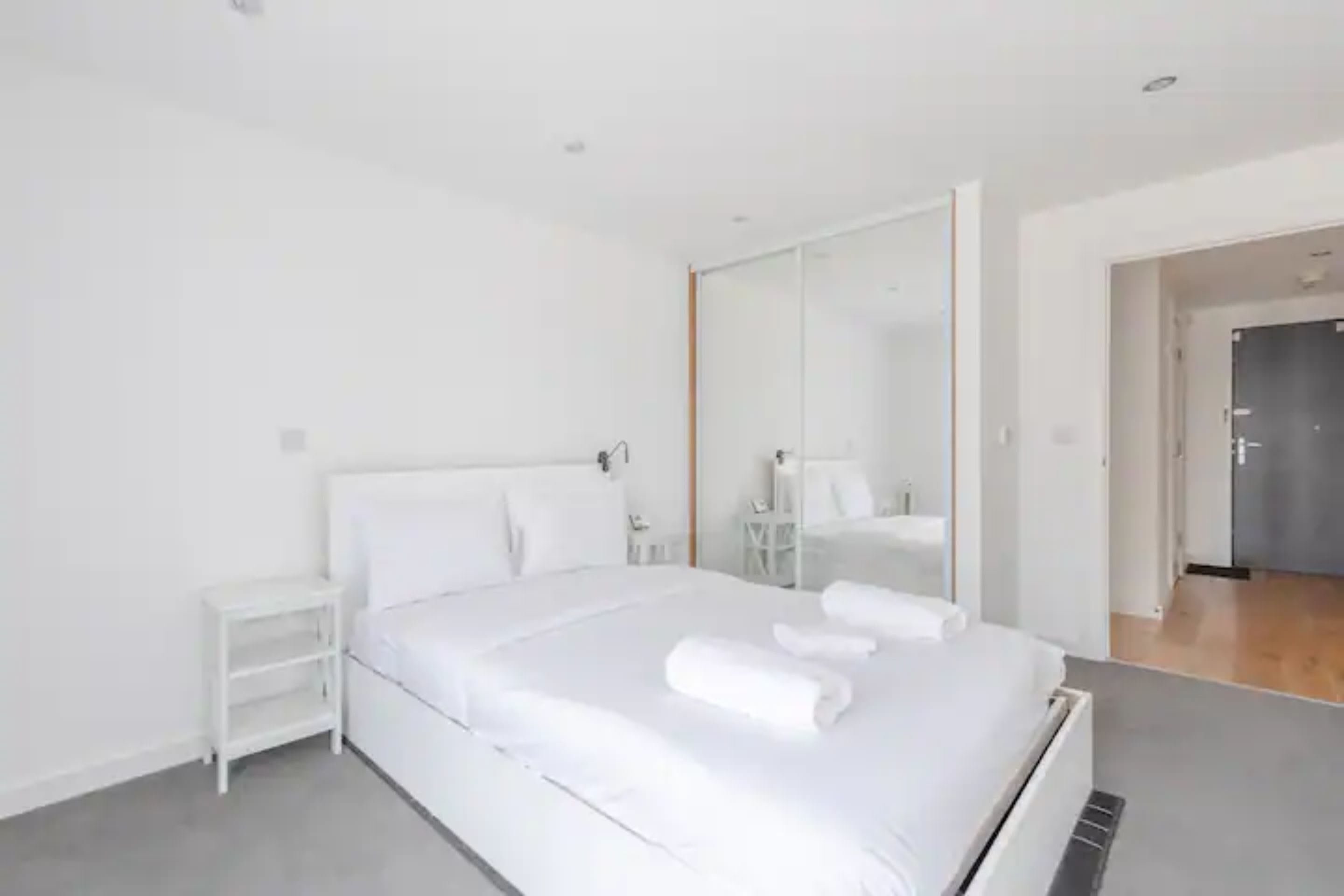 A modern bedroom with a large bed, a nightstand, and a mirror.