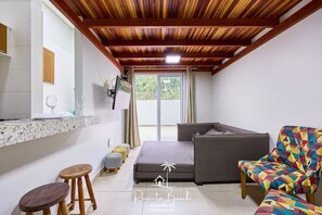 A compact room with a bed, a colorful armchair, a small stool, and a bar area with a counter. - Sunset (Ubatuba)