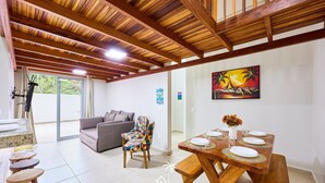 Un salón amplio con techo de madera, una mesa de comedor con platos blancos y un jarrón de flores, una silla colorida y un sofá.