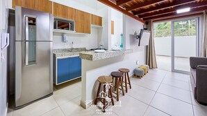 Una cocina moderna con un refrigerador de acero inoxidable, armarios de madera, encimera de granito y un comedor con taburetes.