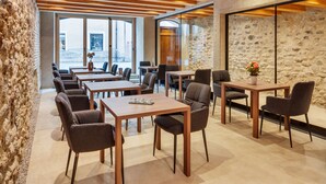 A modern dining area with wooden tables and chairs, stone walls, and large windows offering views of the outside. - Boutiquehotel Rattenberg (Rattenberg)