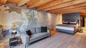 A bedroom with a wooden ceiling, a bed, a sofa, and a nightstand with a lamp. - Boutiquehotel Rattenberg (Rattenberg)