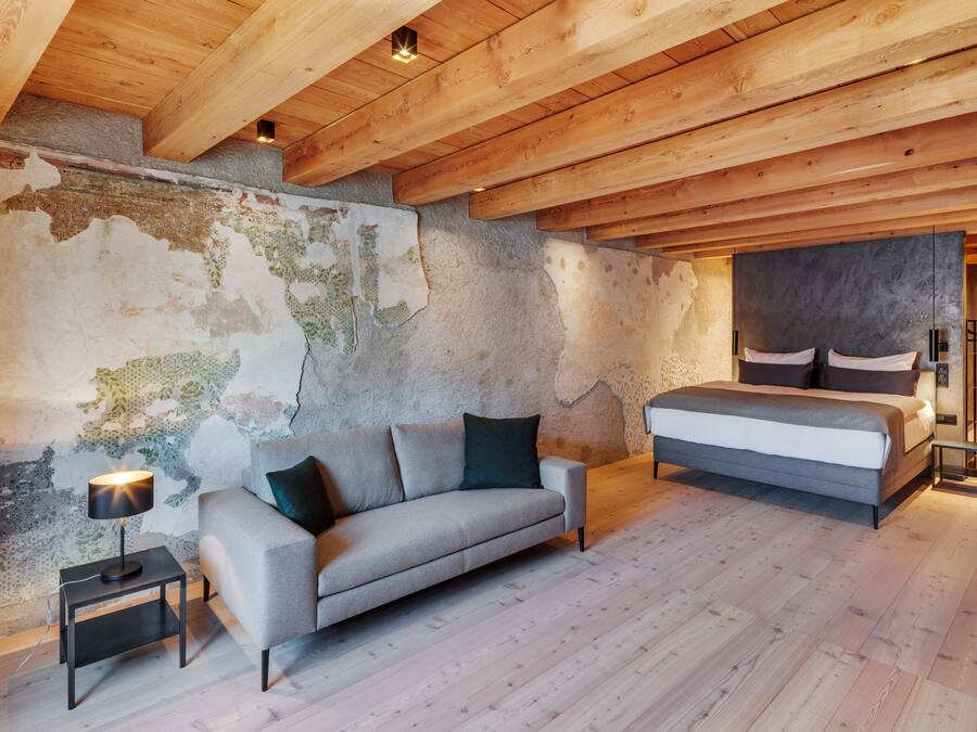 A bedroom with a wooden ceiling, a bed, a sofa, and a nightstand with a lamp.