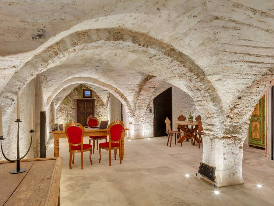 Een eetgedeelte met een rustiek stenen plafond, houten tafels en rode fauteuils.