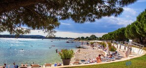 Relax on the beach with lounge chairs and umbrellas, surrounded by lush greenery and a gentle slope leading to the water.