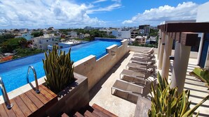 Une piscine sur le toit, avec une eau d’un bleu cristallin, entourée de chaises longues et de plantes en pot.
